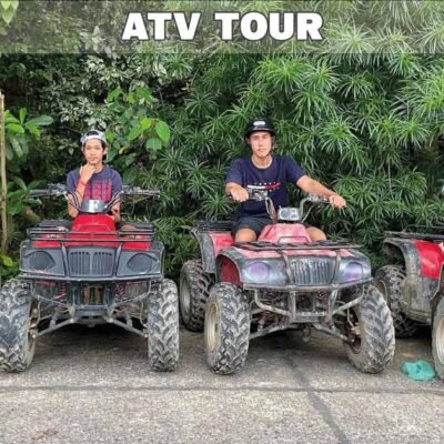 two riders sitting on ATV quad bikes parked side by side with trees in background