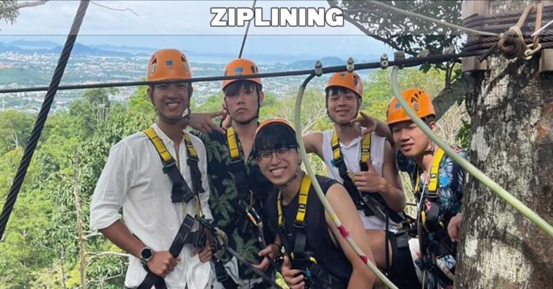 4 smiling customers on zip line in Phuket wearing helmets and harness with zipline in front and lush background