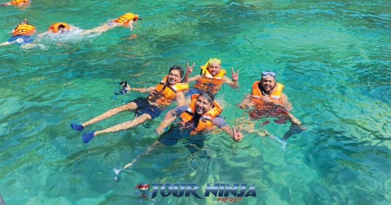best-snorkeling-tours-phi-phi snorkeling tour phi phi with eight participants swimming in the clear blue water wearing orange life jackets and masks and snorkels