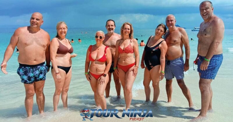 best-snorkeling-tours-phuket snorkeling tour phi phi with a group of nine young males posing for a group photo on a beach with the sea as a backdrop