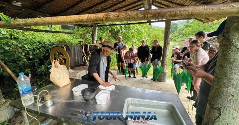 bukit-elephant-food-prep-bu4 bukit elephant park staff member cleans food preparation table in shaded hut while several tourists stand around watching