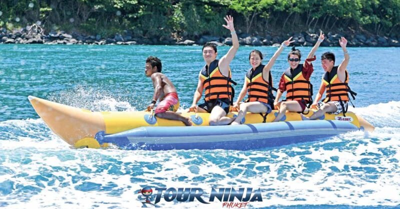 coral-island-daytrip-banana-boat-n2 coral island showing yellow banana boat with five waving customers in orange life jackets with island in background
