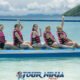 coral island showing yellow banana boat with five smiling girls wearing orange life jackets with island in background