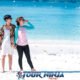 young asian couple standing on beautiful white sandy beach on coral island with crystal clear blue water in background