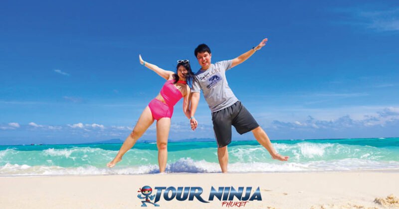 daytrip-phiphi-bamboo-island-s3 bamboo island young asian couple wearing a pink bikini and grey t-shirt and black shorts standing in shallow water