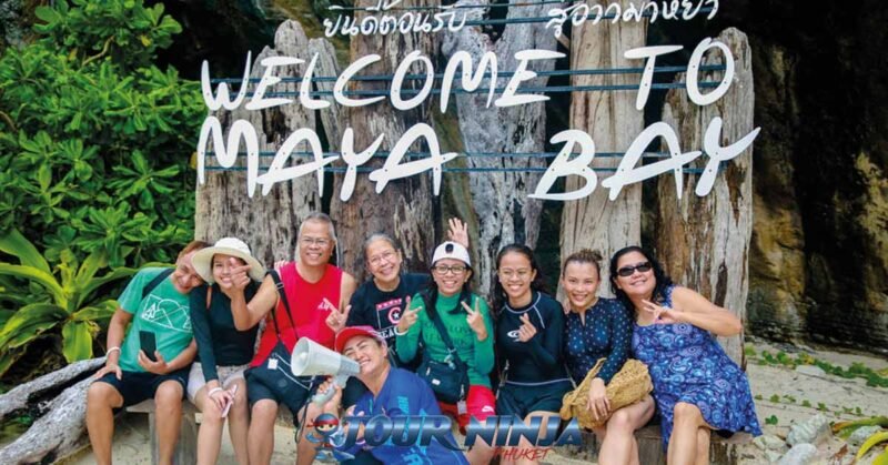 daytrip-phiphi-island-maya-bay-s14 maya bay phi phi island with eight tourist and a tour guide sitting in front of large sign saying welcome to maya bay