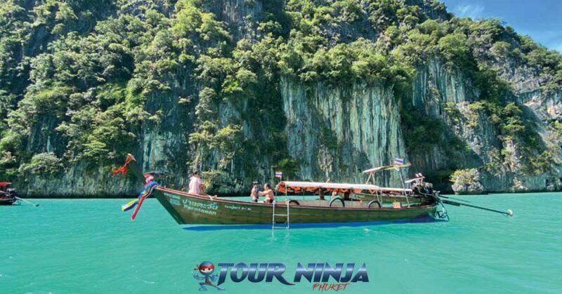 daytrip-phiphi-khai-island-s13 phi phi ley island longtail boat cruising by with a beautiful back drop of limestone rock and a turquoise sea
