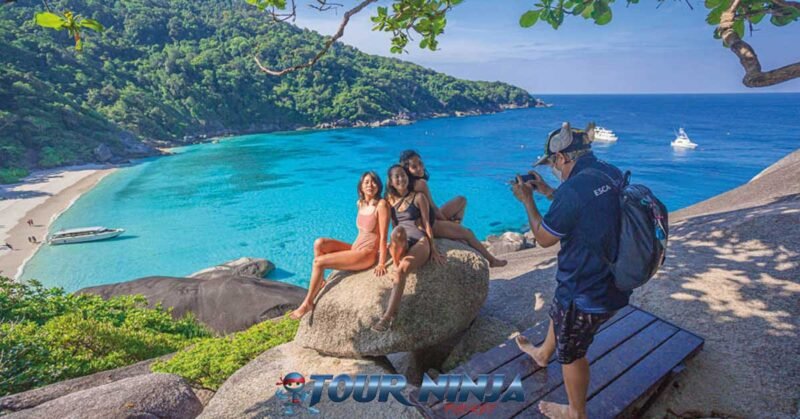 daytrip-similan-island-snorkeling-s8 similan island donald duck bay viewpoint three asian females in swimsuits sitting on a rock being photographed with the bay behind