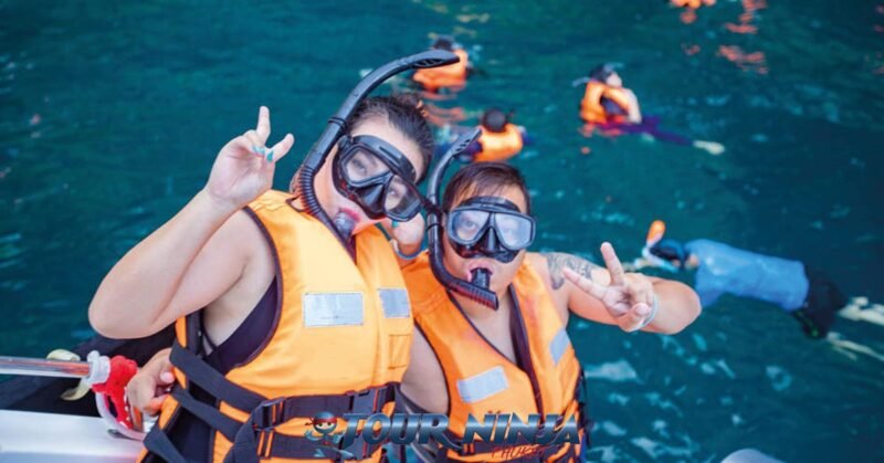 daytrip-snorkeling-bamboo-phiphi-island-s1 phi phi island an asian couple wearing orange lifejackets and black snorkeling gear getting ready to enter the water from a boat