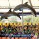 two large dolphins jumps very high up from the pool in front of a large crowd of thai school students