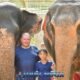 father and son posing with two elephants in rain shower with mahout