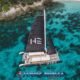 hype luxury sailing catamaran with black sails unfurled viewed from above in emerald sea between two islands