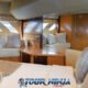 hype luxury cruising yacht master cabin showing large bed with timber paneling and pillows and white bedding and wall mounted white sofa below slanted portholes