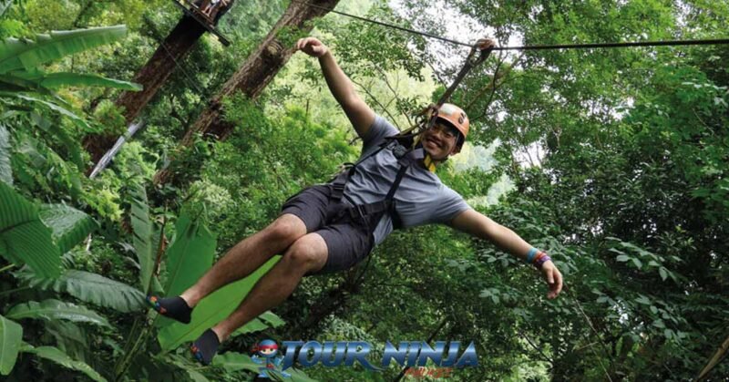 phuket-best-zipling-tours-hw2 eco zipline tour in phuket with a young male wearing a grey shirt and safety gear gliding through the jungle with a big smile