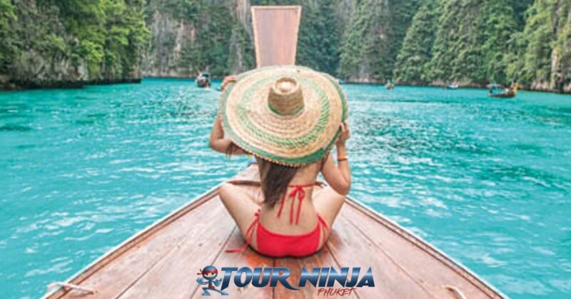 snorkeling-pileh-lagoon-phiphi-island-s9 pileh lagoon phi phi island with a female wearing a large brimmed straw hat and red bikini sitting at the bow of a longtail boat