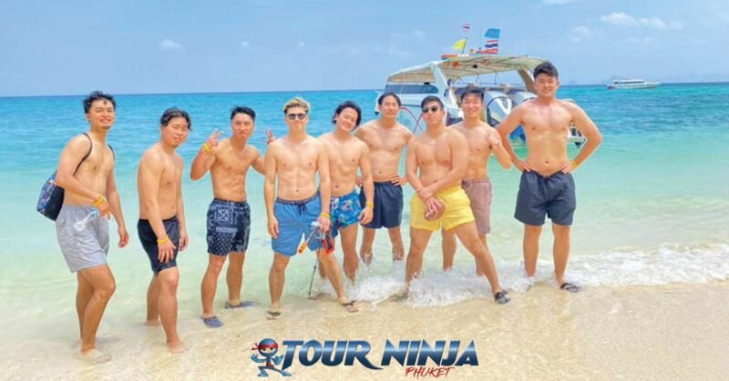 snorkeling-tours-phuket-2 snorkeling with a group of nine young males posing for a group photo on a beach with the sea as a backdrop