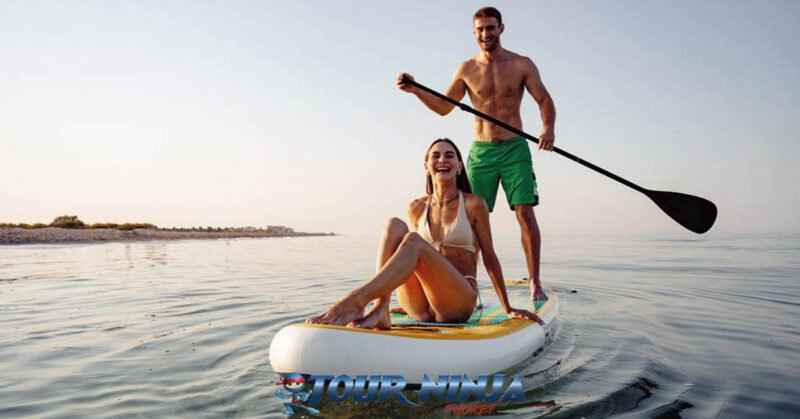 snorkeling-tours-phuket snorkeling tour phuket with a young couple on a standup paddle board the male is standing paddling the female sits in the bow