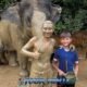 mud covered elephant guide poses with young boy in front of muddy elephant in phuket sanctuary